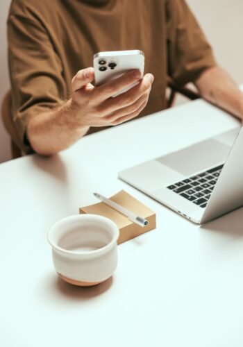 Person interacting with smartphone at tidy desk with laptop and coffee mug, showcasing modern technology.
